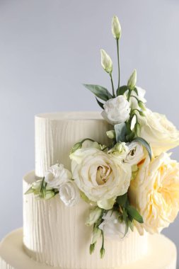 Gri arka planda çiçeklerle süslenmiş lezzetli düğün pastası, yakın plan.