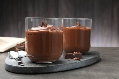 Lezzetli puding ve çikolata parçaları gri masada, yakın plan.