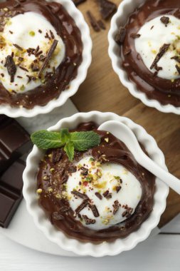 Krem şantili lezzetli puding, beyaz ahşap masa üzerinde çikolata ve kaşık parçaları, düz yatıyordu