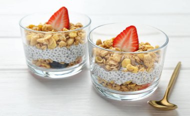 Chia tohumlu lezzetli tatlı, yoğurt, granola ve beyaz ahşap masadaki bardaklarda çilek, yakın plan. Süper yemek.