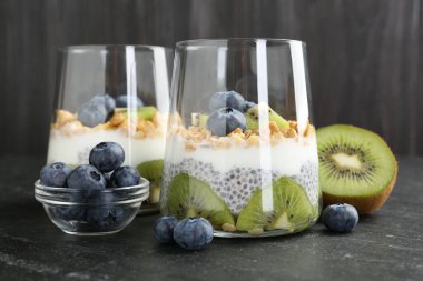 Chia tohumlu lezzetli tatlı, yoğurt, granola, yaban mersini ve kivi siyah masada, yakın plan. Süper yemek.