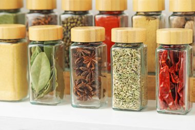 Beyaz masadaki kavanozlardaki farklı aromatik baharatlar, yakın plan.