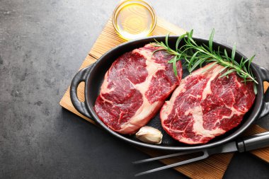 Fırın kabında baharatlı çiğ et parçaları, gri desenli masa üzerinde yağ ve çatal, düz yatar.