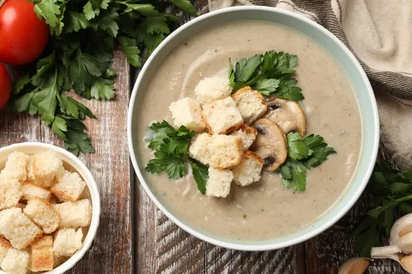 Lezzetli mantar kremalı çorba, kızarmış ekmek ve ahşap masadaki malzemeler.