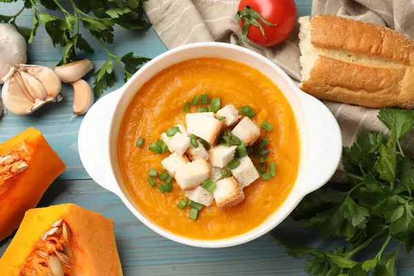 Lezzetli balkabağı kremalı çorba ve yeşil soğan kasede diğer ürünler arasında açık mavi ahşap masa, düz yatıyordu