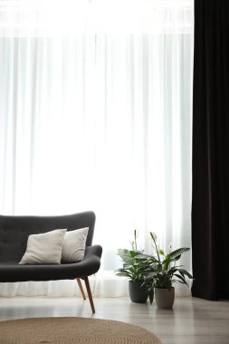 Pencerenin yanında rahat bir kanepe, odada zarif perdeler var.