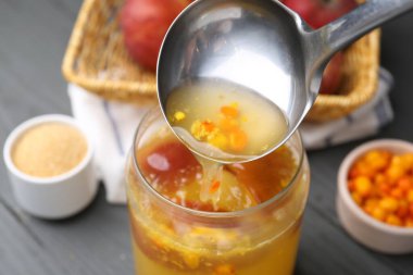 Gri ahşap masada cam kavanoza lezzetli bir şey dökülüyor, yakın plan.