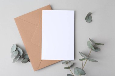Boş tebrik kartı, kağıt zarf ve okaliptüs yaprakları açık gri arka planda, düz yatıyordu.