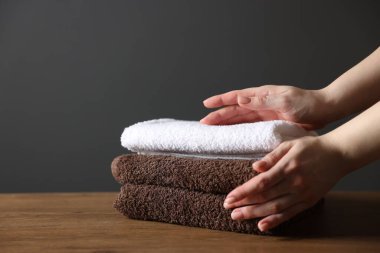 Ahşap masadaki temiz havluları olan kadın koyu gri arka planda, yakın plan.