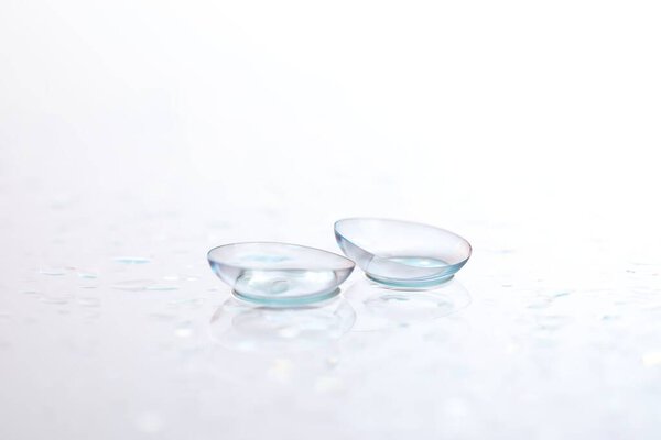 Pair of contact lenses and water drops on white mirror surface, closeup