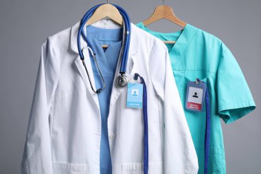 Steteskop ve rozetli sağlık görevlileri gri arka planda askı takıyor.
