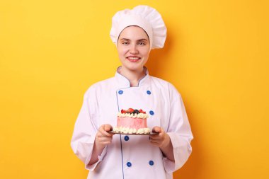 Üniformalı pastacı turuncu arka planda lezzetli bir pasta tutuyor.