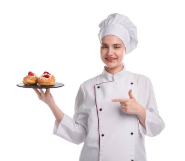 Üniformalı mutlu pastacı beyaz arka planda çilekli lezzetli profiteroller tutuyor.