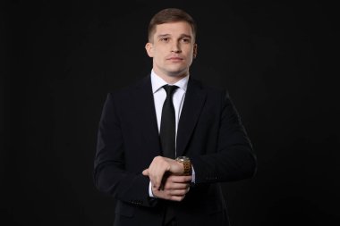 Siyah arka planda şık saati olan klasik takım elbiseli bir adam.