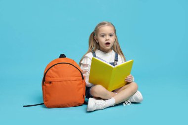 Sırt çantası ve açık mavi arka plan kitabı olan tatlı bir kız öğrenci.