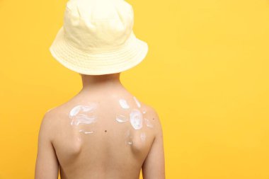 Cildinde güneş kremi olan küçük bir çocuk sarı arka plan, arka plan. Metin için boşluk