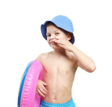 Şişme yüzüklü küçük çocuk beyaz arka planda cildine güneş kremi sürüyor.