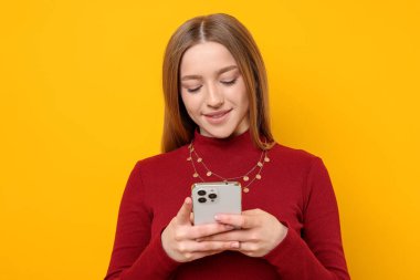 Sarı arka planda akıllı telefonu olan gülümseyen genç kız.