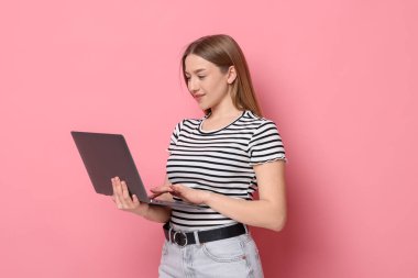 Pembe arka planda dizüstü bilgisayarı olan gülümseyen genç kız.
