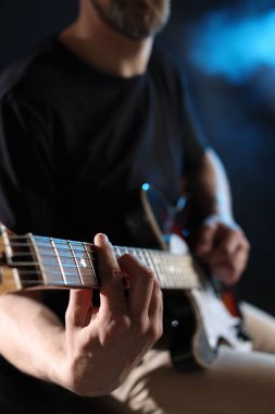 Karanlık arka planda gitar çalan adam dumanlı, eline odaklan