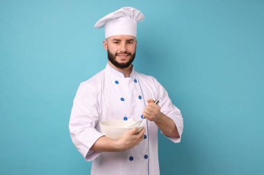 Üniformalı mutlu pastacı elinde çırpı ve kase ile açık mavi arka planda