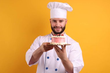 Üniformalı mutlu pastacı elinde turuncu arka planda böğürtlen tutuyor.