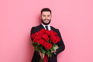 Pembe arka planda kırmızı güller açan mutlu bir adam.