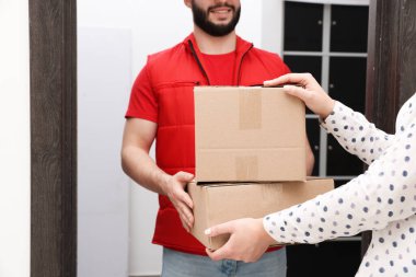 Gülümseyen kurye kapalı alanda alıcıya paketler veriyor, yakın plan.