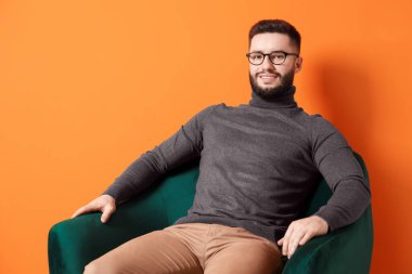 Gülümseyen adam turuncu arka planda koltukta dinleniyor.