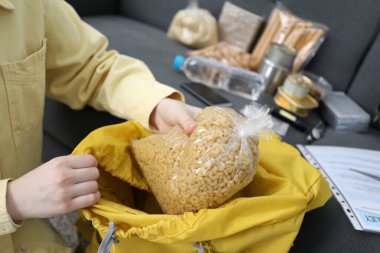 Hayatta kalma kiti. Kadın içeride sırt çantasına çiğ makarna koyuyor.