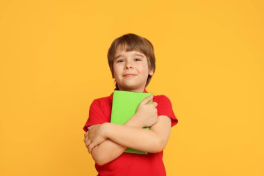 Turuncu arka plan kitabı olan küçük bir çocuk.