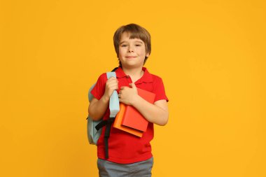 Turuncu arka planda kitapları ve sırt çantası olan küçük bir çocuk.
