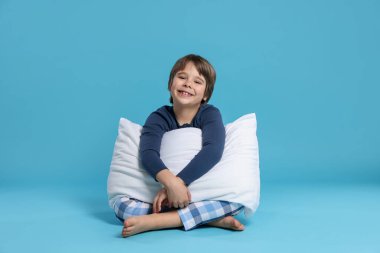 Açık mavi arka planda yastığı olan sevimli bir çocuk.