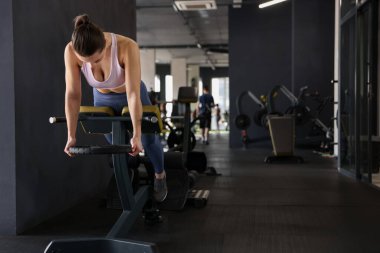 Spor salonundaki T-Bar sıra makinesinde ağırlık plakalı atletik kadın antrenmanı. Metin için boşluk