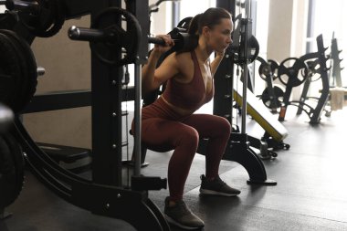 Spor salonunda Smith makinesinde halterli kadın antrenmanı