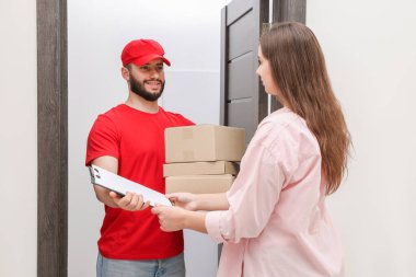 Paketlerle gülümseyen kurye kapalı alandaki alıcıya pano veriyor