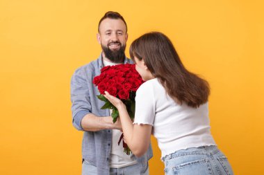 Adam turuncu arka planda sevgilisine kırmızı gül buketi sunuyor.