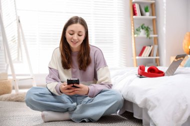 Genç kız evde yerde akıllı telefon kullanıyor.