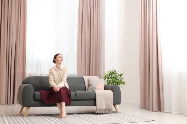 Kadın pencerenin yanındaki kanepede oturuyor ve evinde şık perdeler var. Metin için boşluk