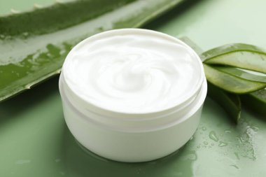 Aloe vera özütüyle nemlendirici krem, yeşil arkaplanda yapraklar ve su damlaları, yakın plan