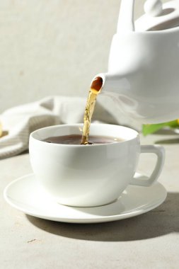 Hafif desenli masada çaydanlıktan fincana aromatik çay dökülüyor, yakın plan.