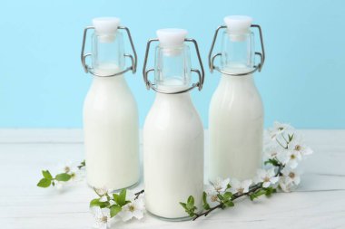 Taze süt ve çiçekler beyaz masada açık mavi arka planda