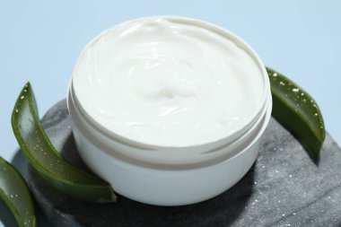 Aloe vera özütüyle nemlendirici krem ve açık mavi arkaplanda yapraklar, yakın plan.