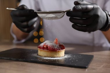 İçerideki ahşap masadaki turtaya şeker serpiştiren şekerci, yakın plan.