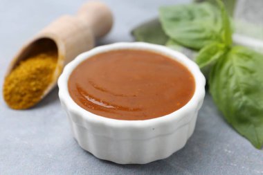 Lezzetli köri sosu, toz ve fesleğen yaprakları gri masada, yakın plan.