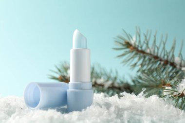 Nemlendirici dudak kremi ve yapay kar üzerindeki köknar ağacı dalları açık mavi arka planda, yakın plan. Kış bakımı