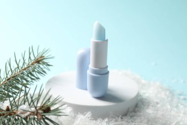 Nemlendirici dudak kremi ve yapay kar üzerindeki köknar ağacı dalları açık mavi arka planda, yakın plan. Kış bakımı