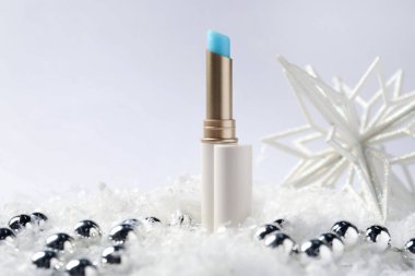 Nemlendirici dudak kremi ve yapay kar üzerindeki Noel süsü beyaz arka planda, yakın plan. Kış bakımı