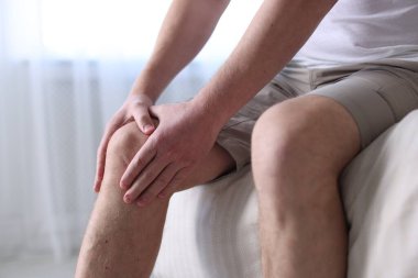 Evdeki yatakta diz ağrısı çeken bir adam, yakın plan.