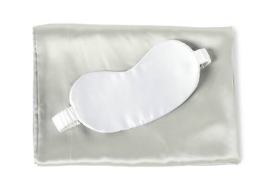 Beyaz arka planda ipek çarşaflar ve uyku maskesi, üst manzara.